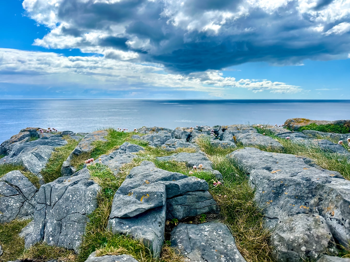 Rocky coastal landscape on Inishmore, Ireland, with grassy stone textures, ocean horizon, and dramatic clouds overhead.