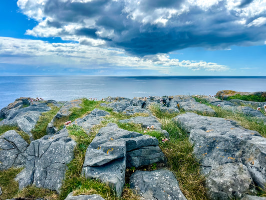 Rocky coastal landscape on Inishmore, Ireland, with grassy stone textures, ocean horizon, and dramatic clouds overhead.