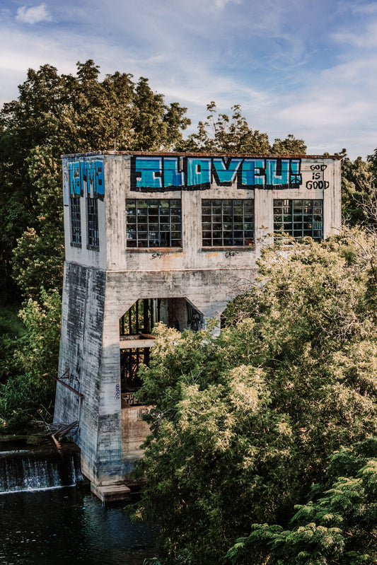 Weathered Faust Street Bridge area structure in New Braunfels, Texas, with old windows, graffiti, trees, and water below.