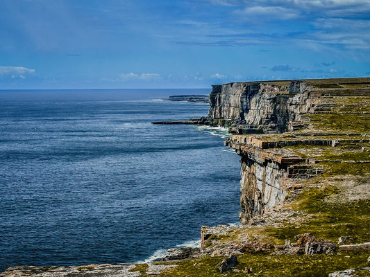 Dramatic coastal cliffs on Inishmore, Ireland, overlooking deep blue ocean water with rugged stone textures and open sky.