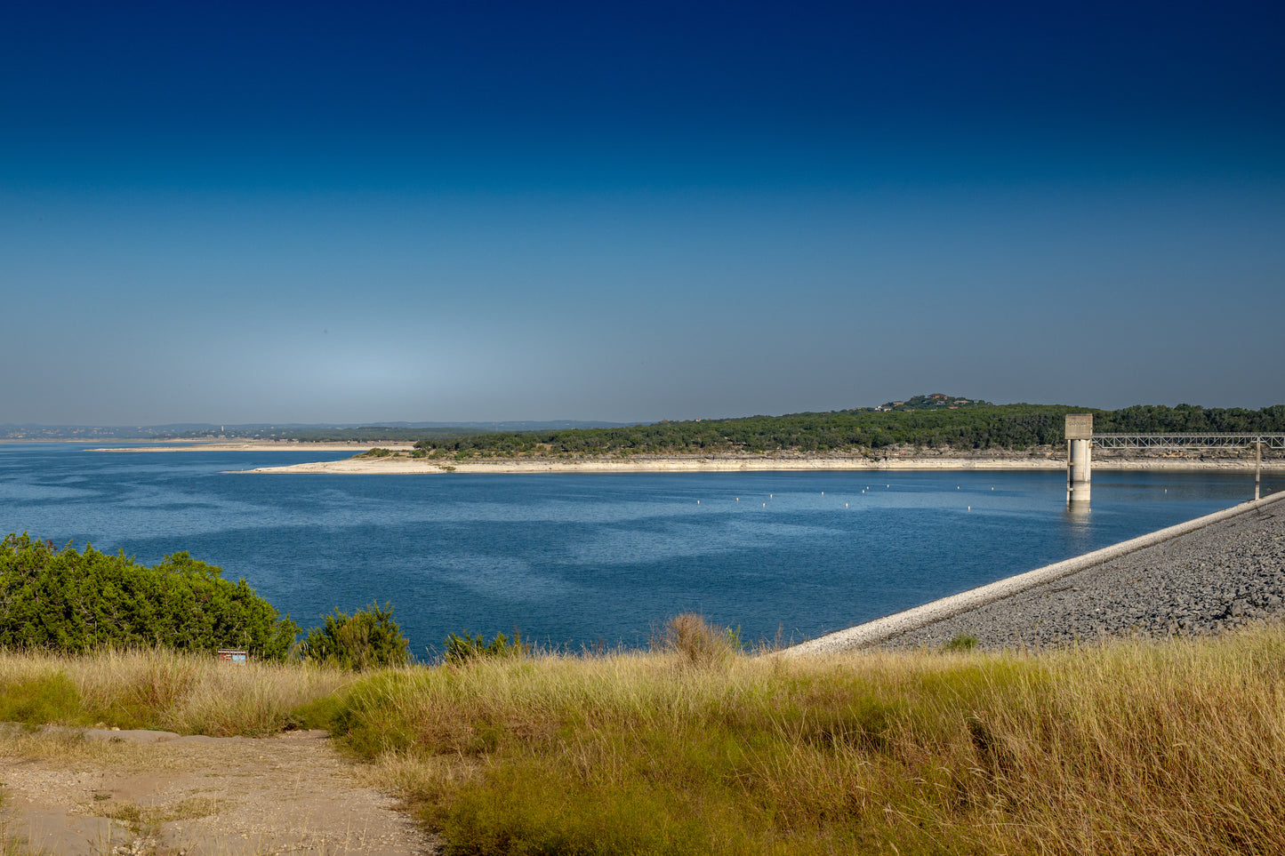 Canyon Lake Dam area in Texas with deep blue water, shoreline grasses, open sky, and peaceful Hill Country scenery.