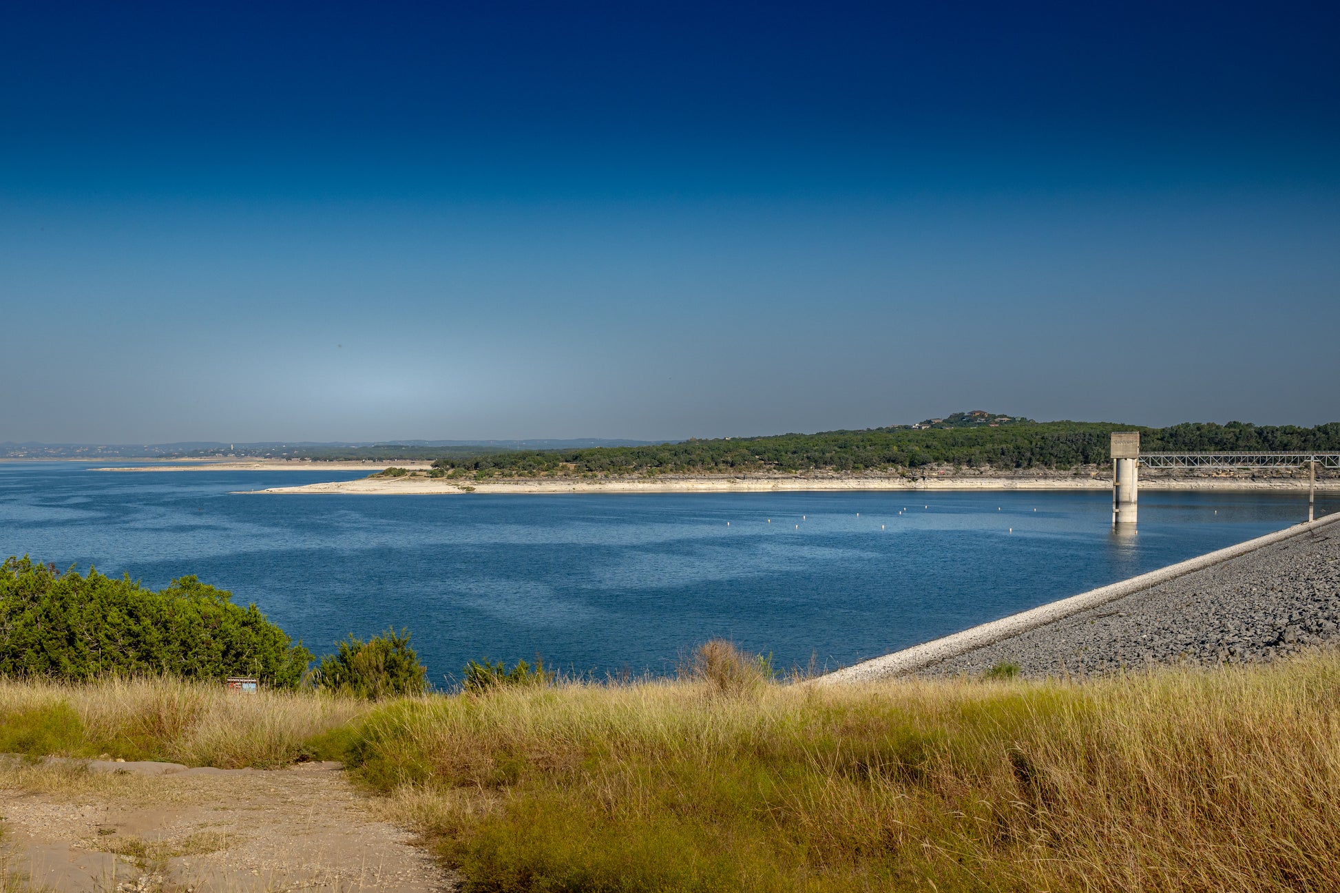 Canyon Lake Dam area in Texas with deep blue water, shoreline grasses, open sky, and peaceful Hill Country scenery.