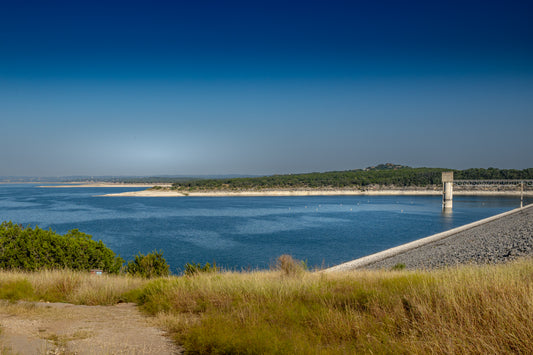 Canyon Lake Dam area in Texas with deep blue water, shoreline grasses, open sky, and peaceful Hill Country scenery.