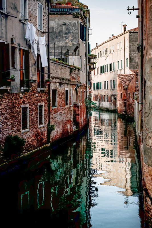 Quiet canal in Venice, Italy, lined with weathered brick buildings and soft reflections in the water.