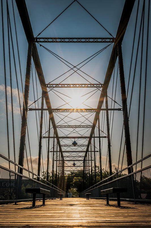 View from inside the historic Faust Street Bridge in New Braunfels, Texas, with strong metal lines, wooden walkway, and warm sunlight.